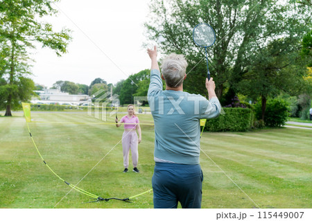 Focus om man with racket playing badminton with young woman in the park. Friends having fun and training outdoors. Enjoying game and natural environment. Adult Outdoor activity. Healthy lifestyle. Focus om man with racket playing badminton with young woman in the park. Friends having fun and training outdoors. Enjoying game and natural environment. Adult Outdoor activity. Healthy lifestyle. 115449007