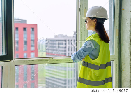 Back view of female industrial worker in protective helmet vest looking at new buildings Back view of female industrial worker in protective helmet vest looking at new buildings 115449077