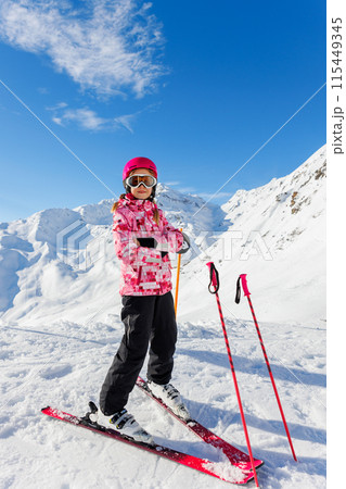Active confident adorable teenager caucasian kid girl portrait with ski in helmet, goggles and bright suit enjoy winter extreme sport activities. Little child skiing luxury alpine resort in mountains Active confident adorable teenager caucasian kid girl portrait with ski in helmet, goggles and bright suit enjoy winter extreme sport activities. Little child skiing luxury alpine resort in mountains 115449345