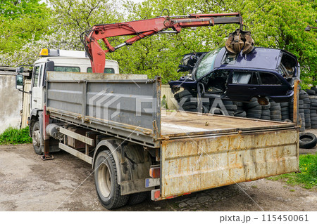 A hydraulic loader loads a abandoned car wreck onto a truck to take it to a recycling site 115450061