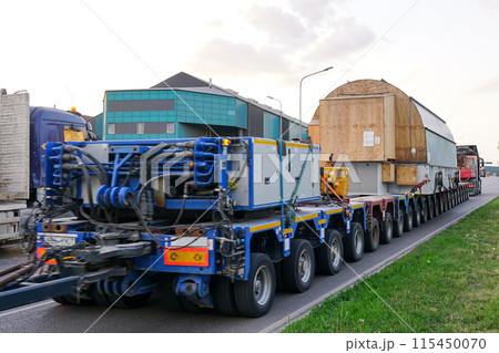 Very long specialized multi axle truck trailer carries very heavy oversize load, rear view 115450070