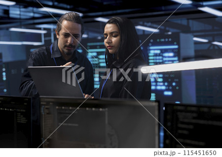 Programmers in server room checking recovery plan, monitoring tech gear energy consumption using notebook. Colleagues in data center workplace doing routine disk checks using laptop and tablet Programmers in server room checking recovery plan, monitoring tech gear energy consumption using notebook. Colleagues in data center workplace doing routine disk checks using laptop and tablet 115451650