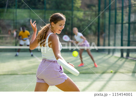 Sportive slim woman with racquet playing padel in court. View from back Sportive slim woman with racquet playing padel in court. View from back 115454001