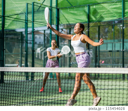 Girl jumping while playing padel tennis match during training on court Girl jumping while playing padel tennis match during training on court 115454028