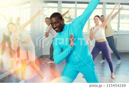 African american man and group of young active sports people practicing rock and roll dance in dance hall African american man and group of young active sports people practicing rock and roll dance in dance hall 115454289