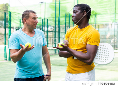 Men chatting on outdoor padel tennis court 115454468