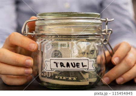 Unrecognizable woman holding Saving Money In Glass Jar filled with Dollars banknotes. TRAVEL transcription in front of jar. Managing personal finances extra income for future insecurity Unrecognizable woman holding Saving Money In Glass Jar filled with Dollars banknotes. TRAVEL transcription in front of jar. Managing personal finances extra income for future insecurity 115454945
