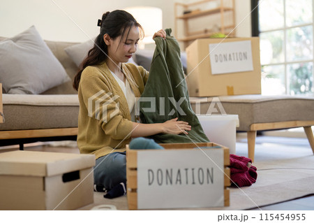 Volunteer Sorting and Donation Clothes for Charity in a Modern Living Room Setting, Highlighting Community Support and Generosity 115454955