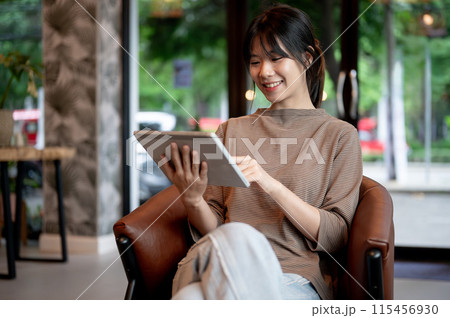 A pretty, positive young Asian woman using her digital tablet in a coffee shop. A pretty, positive young Asian woman using her digital tablet in a coffee shop. 115456930