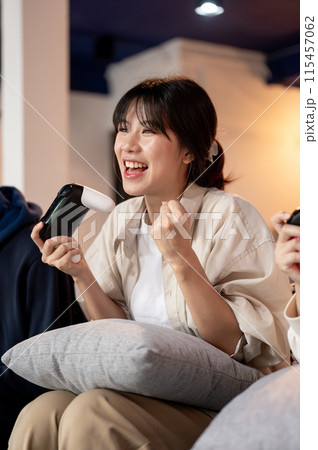 A young, cheerful Asian girl is enjoying playing a video game with her friends at home. 115457062