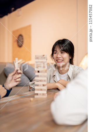 A happy Asian woman is playing wooden blocks at home, watching her friend remove a wooden block. 115457082