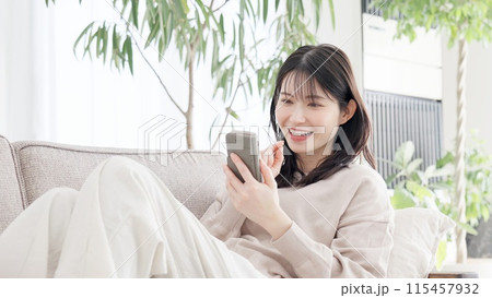ソファでくつろぎながらスマホを見る女性 115457932