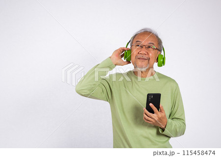 Portrait Asian smiling old man wearing glasses and headphones is holding smartphone listen music in headphones studio shot isolated on white background, enjoying his music 115458474