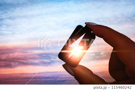 Hand holding energy symbol at dawn, electric power concept with sunrise sky, renewable energy icon in silhouette, sustainable resources representation 115460242