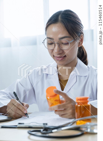 Female doctor holding a medicine bottle is checking the quality of medicine for any side effects the patient or not and recording patient information at the hospital. medical and health care concept Female doctor holding a medicine bottle is checking the quality of medicine for any side effects the patient or not and recording patient information at the hospital. medical and health care concept 115460514