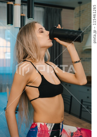 Woman Drinking From Black Water Bottle After Workout in Kitchen 115461265