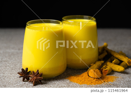 Golden milk, a traditional Ayurvedic drink with turmeric in two glasses on a black gray background 115461964