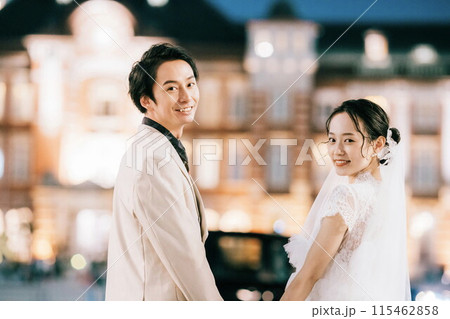 夜の東京駅をバックに振り返る新郎新婦 115462858