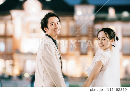 夜の東京駅をバックに振り返る新郎新婦 115462859