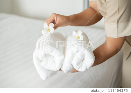 A hotel maid stacked towels on the bed and placed flowers on the towels in a hotel room A hotel maid stacked towels on the bed and placed flowers on the towels in a hotel room 115464376