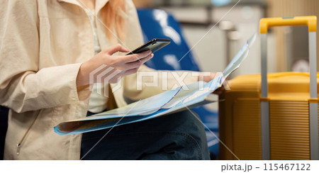 Young Woman at Airport with Luggage and Map, Using Smartphone for Travel Planning and Navigation, Modern Travel Concept, Solo Female Traveler, Exploring New Destinations, Travel Preparation 115467122