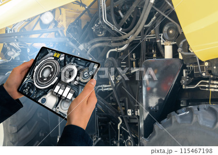 Serviceman with digital tablet next to combine harvester with open hood. 115467198