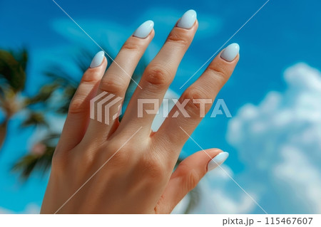 Close-up of a woman's manicured hand against a blue sky background 115467607