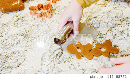 Using various festive cookie cutters, we're cutting out charming gingerbread cookies from the rolled dough on the sleek marble counter, bringing holiday cheer to the modern kitchen. Using various festive cookie cutters, we're cutting out charming gingerbread cookies from the rolled dough on the sleek marble counter, bringing holiday cheer to the modern kitchen. 115468771