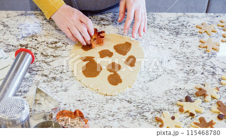 Using various festive cookie cutters, we're cutting out charming gingerbread cookies from the rolled dough on the sleek marble counter, bringing holiday cheer to the modern kitchen. 115468780
