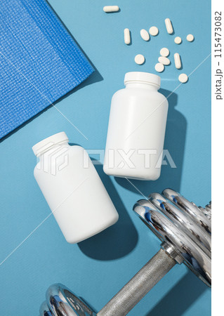 White plastic jars with pills and sport equipment on blue background, top view White plastic jars with pills and sport equipment on blue background, top view 115473082