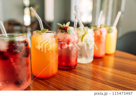 Fruit drinks with berries and ice in glass glasses and straws on a wooden table 115473497