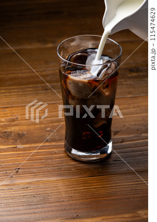 氷とアイスコーヒーの入ったグラスにミルクを注ぐ 115474629