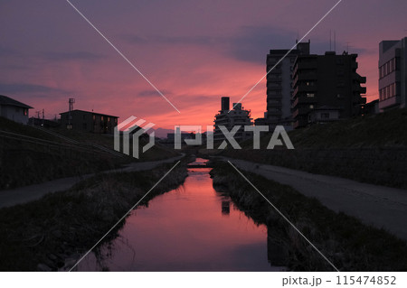 夕焼けに染まる住宅街の川 115474852