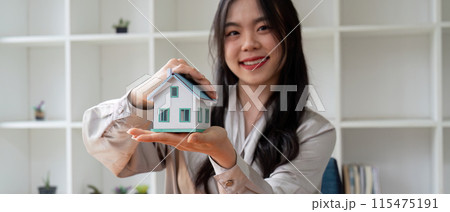 Smiling Woman Holding Miniature House Model in Hands, Real Estate Agent Promoting Property Sale, Modern Home Concept, Professional Realtor Offering New Home, Real Estate Investment Opportunity Smiling Woman Holding Miniature House Model in Hands, Real Estate Agent Promoting Property Sale, Modern Home Concept, Professional Realtor Offering New Home, Real Estate Investment Opportunity 115475191