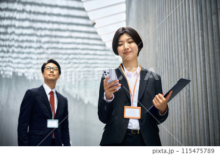 社内を移動中にスマホを操作するスーツのビジネスウーマン 社内を移動中にスマホを操作するスーツのビジネスウーマン 115475789