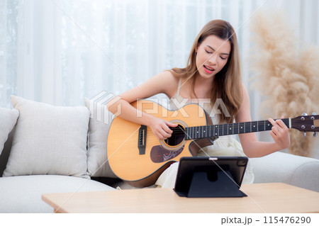 Young asian woman sitting on sofa looking tablet for practice music with guitar in living room. Young asian woman sitting on sofa looking tablet for practice music with guitar in living room. 115476290