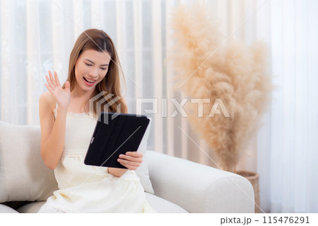 Young asian woman sitting on sofa using digital tablet computer for video call in living room. 115476291