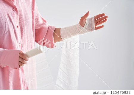 A woman in a pink shirt holds a bandage and puts a bandage on her arm. 115476922