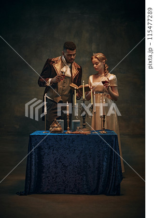 Cozy evening atmosphere. Elegant young woman and handsome man, royal family standing by the table with candles, drinking wine and reading books 115477289