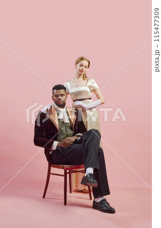 Classical noble portrait of regal gentleman in rich velvet coat, with lady standing confidently behind him against pink studio background Classical noble portrait of regal gentleman in rich velvet coat, with lady standing confidently behind him against pink studio background 115477309