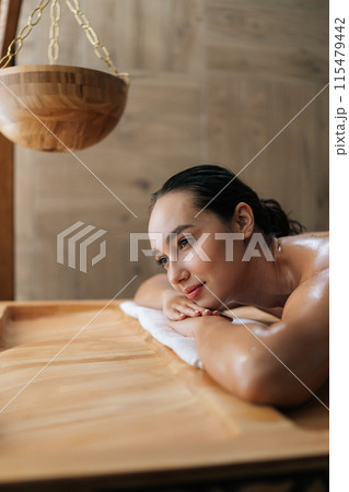 Closeup vertical portrait of young woman in wellness center waiting for massage therapy. Portrait of beautiful female lying down on massage table at spa salon. Happy lady awaiting beauty treatment. 115479442