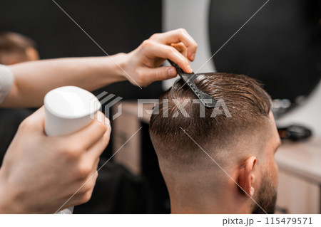 A barber sprays and combs mans hair at the barbershop.  115479571