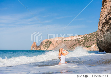 Happy woman in bikini sits on the sea beach. Tanned girl sunbathing on a beautiful shore. Summer vacation or holiday travel concept 115480341