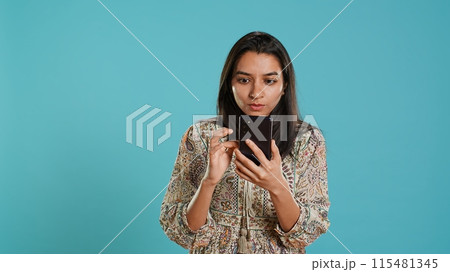 Woman scrolling on smartphone screen, doing online shopping, amazed by beautiful clothes. Portrait of relaxed person browsing internet websites, exclaiming in astonishment, studio background, camera A Woman scrolling on smartphone screen, doing online shopping, amazed by beautiful clothes. Portrait of relaxed person browsing internet websites, exclaiming in astonishment, studio background, camera A 115481345