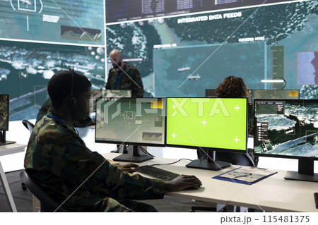 Army personnel monitors isolated green screen and surveillance footage, gathering important battlefield information. Trooper examines CCTV reconnaissance imagery to support soldiers. 115481375