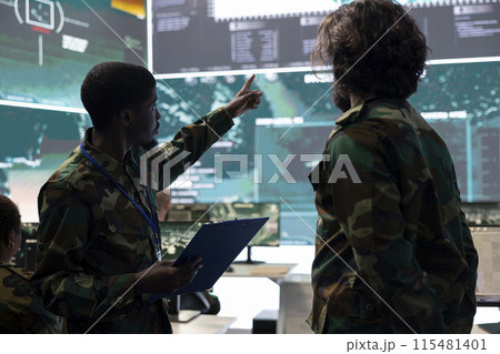 Servicemen working on new national safety plan for an operation, studying the CCTV surveillance system together in military control room. Military personnel analyze satellite support. Servicemen working on new national safety plan for an operation, studying the CCTV surveillance system together in military control room. Military personnel analyze satellite support. 115481401