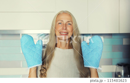 Happy smiling woman housewife with oven gloves potholders is engaged in cooking food in the kitchen 115481623