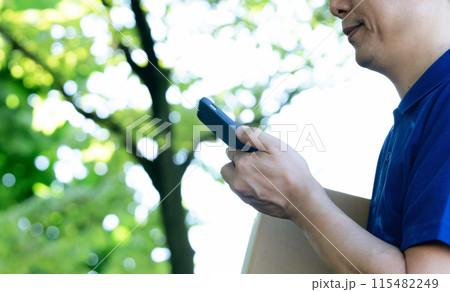 荷物とスマートフォンを持つ男性の手元 荷物とスマートフォンを持つ男性の手元 115482249