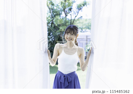カーテンから顔をのぞかせる若い女性 115485162