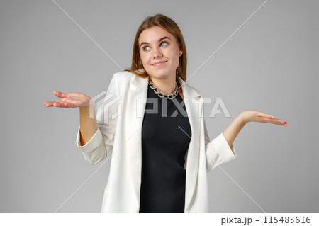 Young Woman Expressing Confusion With Hands Raised Against a Grey Background 115485616